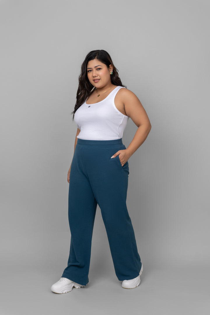 Model wearing a white rib tank top with blue pants.