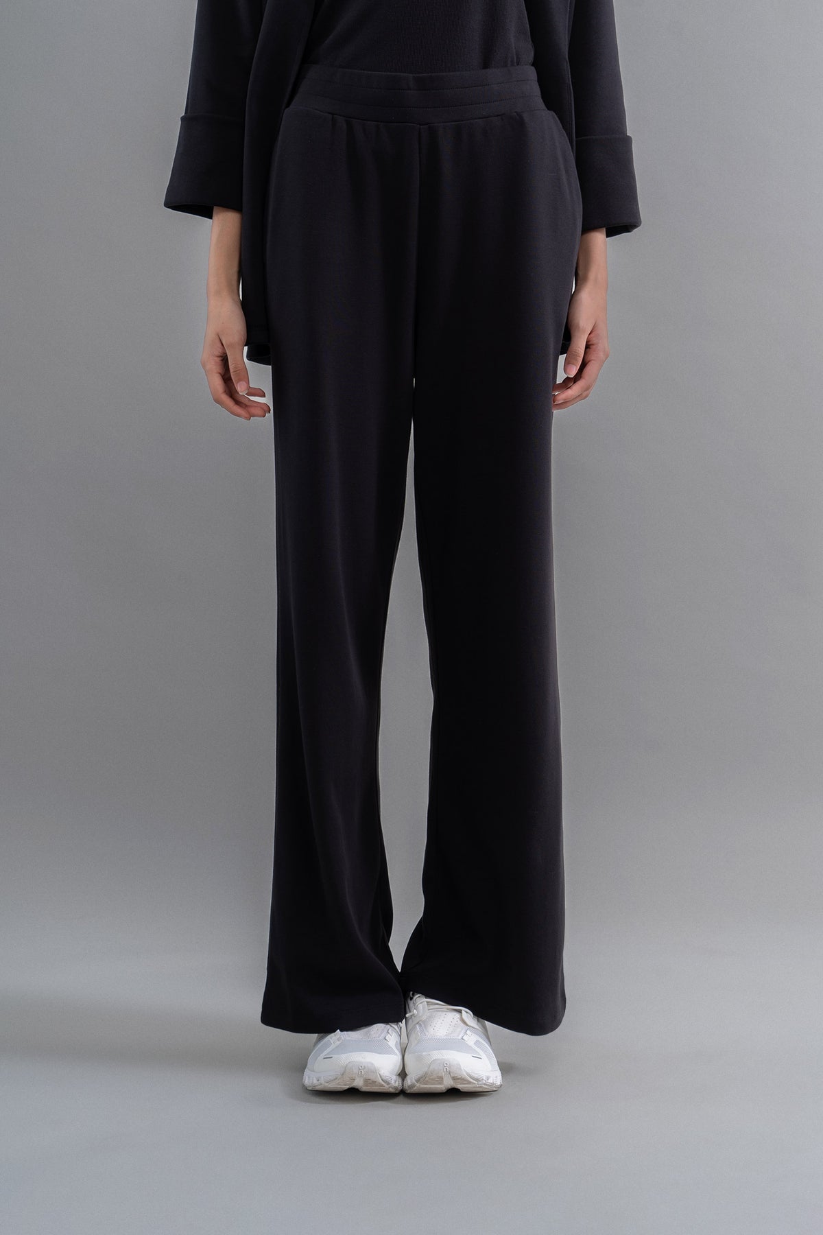 Snugknit® Black Flared Pant worn with white sneakers on a gray background.