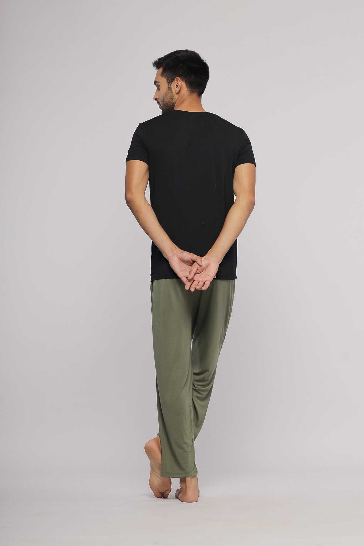 Black men's tee worn with stylish green pants, back view.