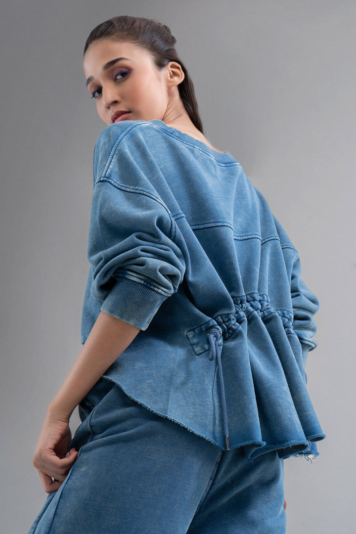 Model wearing denim wash 100% cotton terry ruched sweatshirt from behind.