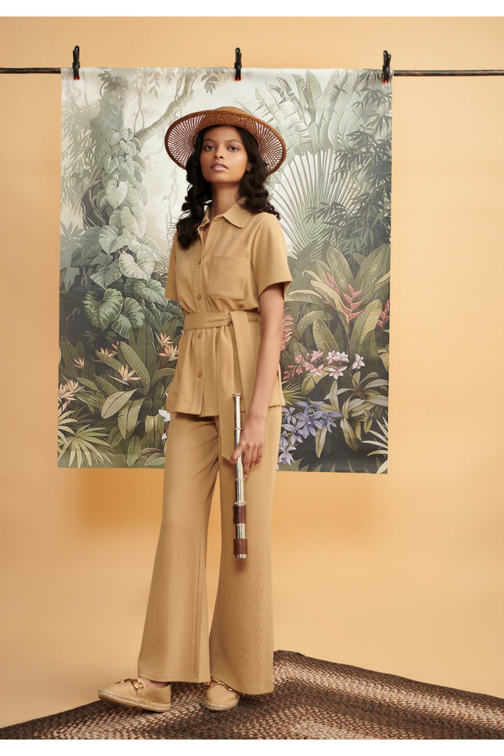 Model wearing mini waffle brown flared pants against a tropical backdrop.