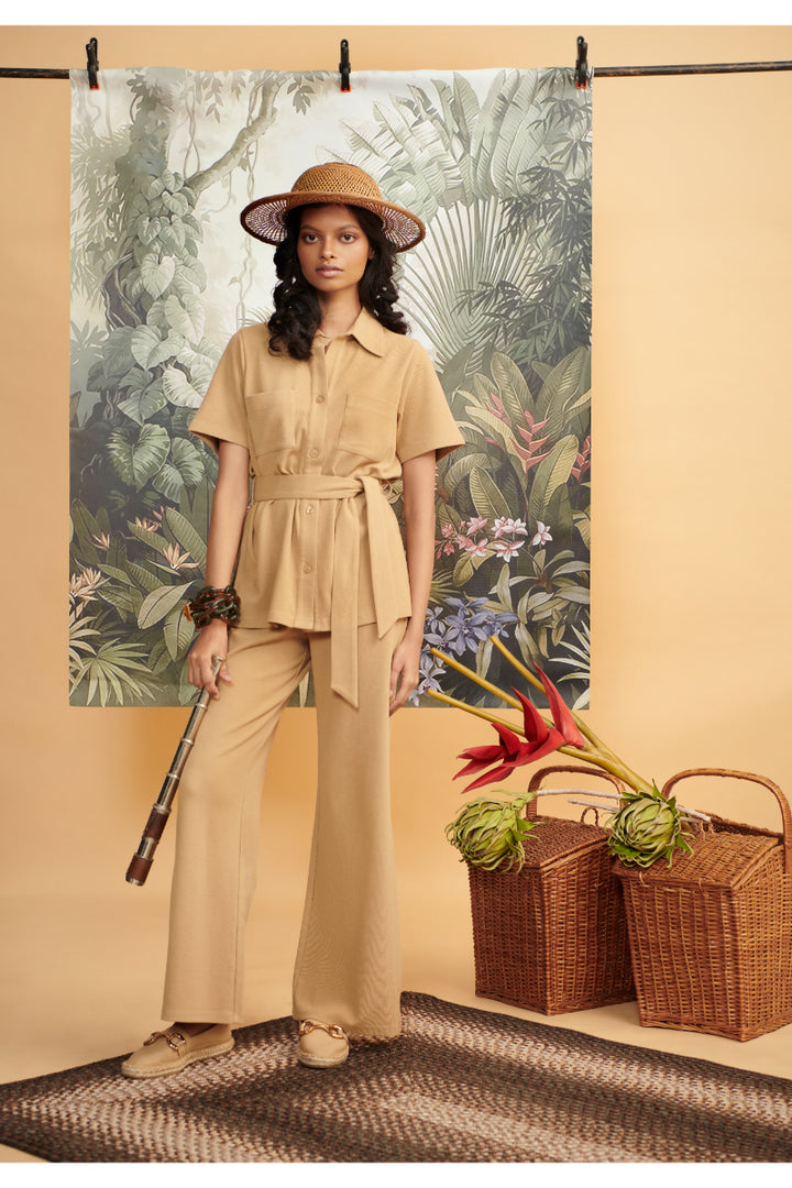"Model wearing Mini Waffle Brown Flared Pants against tropical backdrop."