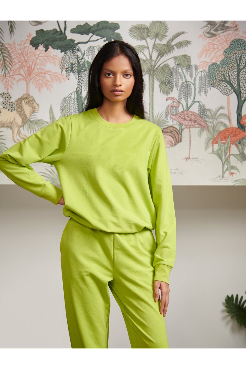 Green bamboo terry sweatshirt model posing against tropical backdrop.
