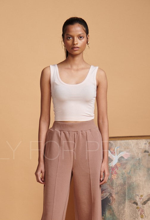 Light pink cropped vest worn with stylish trousers against a warm backdrop.