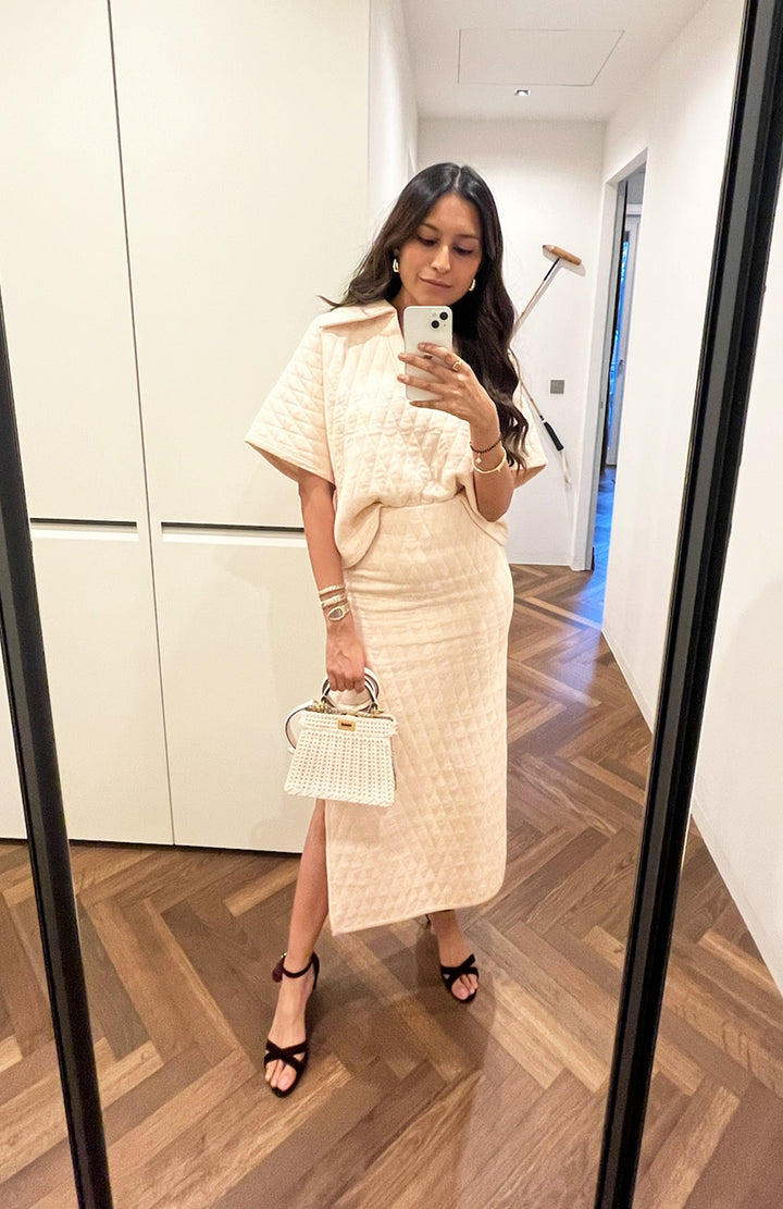 Stylish woman in quilted white skirt set with handbag.