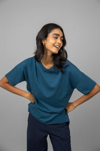 Smiling model wearing teal oversized cotton tee against gray background.