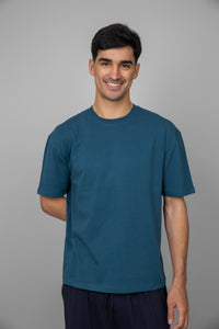 Blue men's oversized tee on smiling model against neutral background.