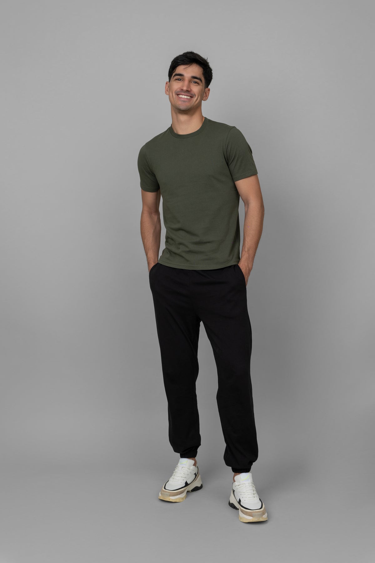 Man smiling in green essential t-shirt, black joggers, and sneakers.