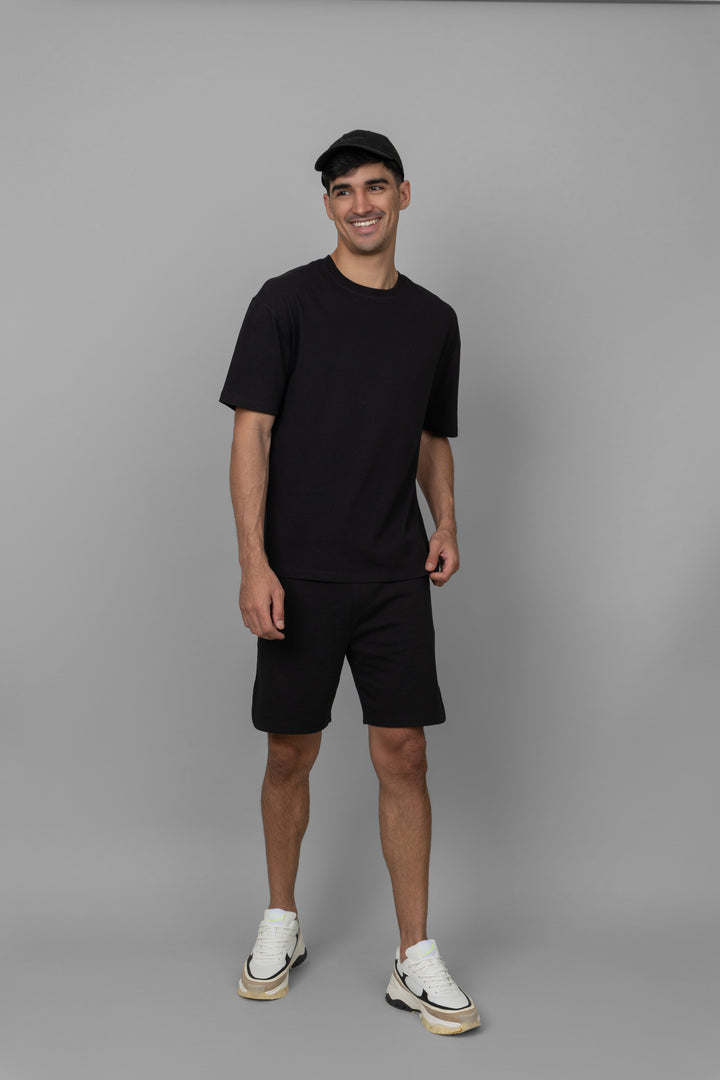 Black men's boxy shorts set styled with sneakers on a neutral background.