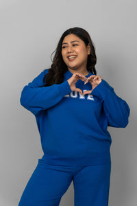 Plus-size model wearing a blue bamboo terry sweatshirt, making a heart shape.