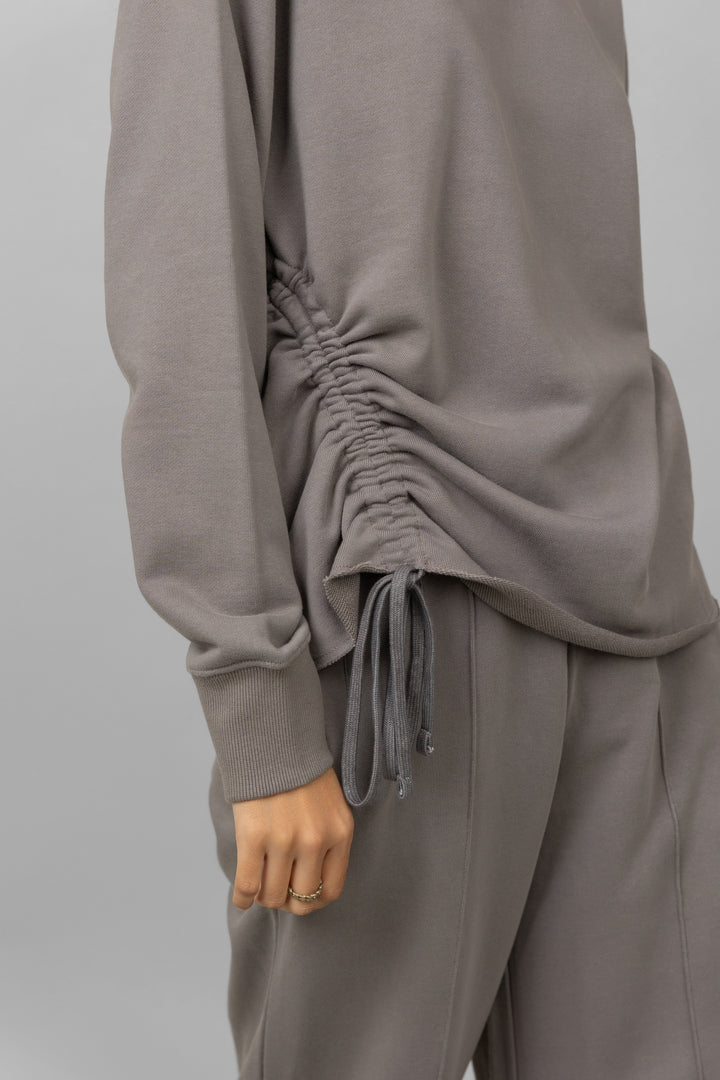 Grey cotton terry sweatshirt with gathered sides and drawstring detail.