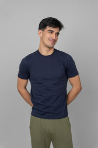 Navy men's essential t-shirt worn by smiling man against gray backdrop.