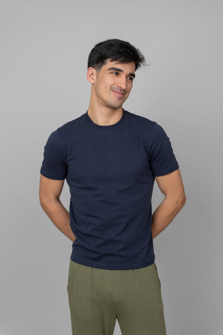 Navy men's essential t-shirt worn by smiling man against gray backdrop.