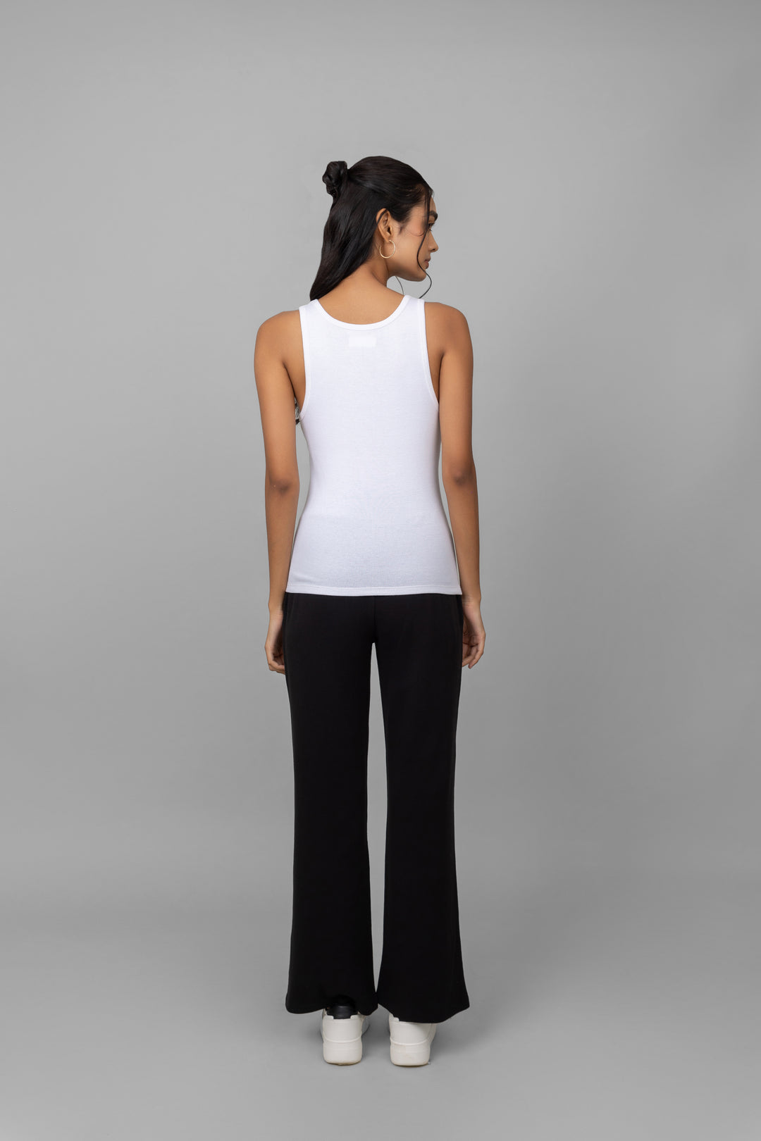 Woman wearing a white ribbed tank top and black joggers.