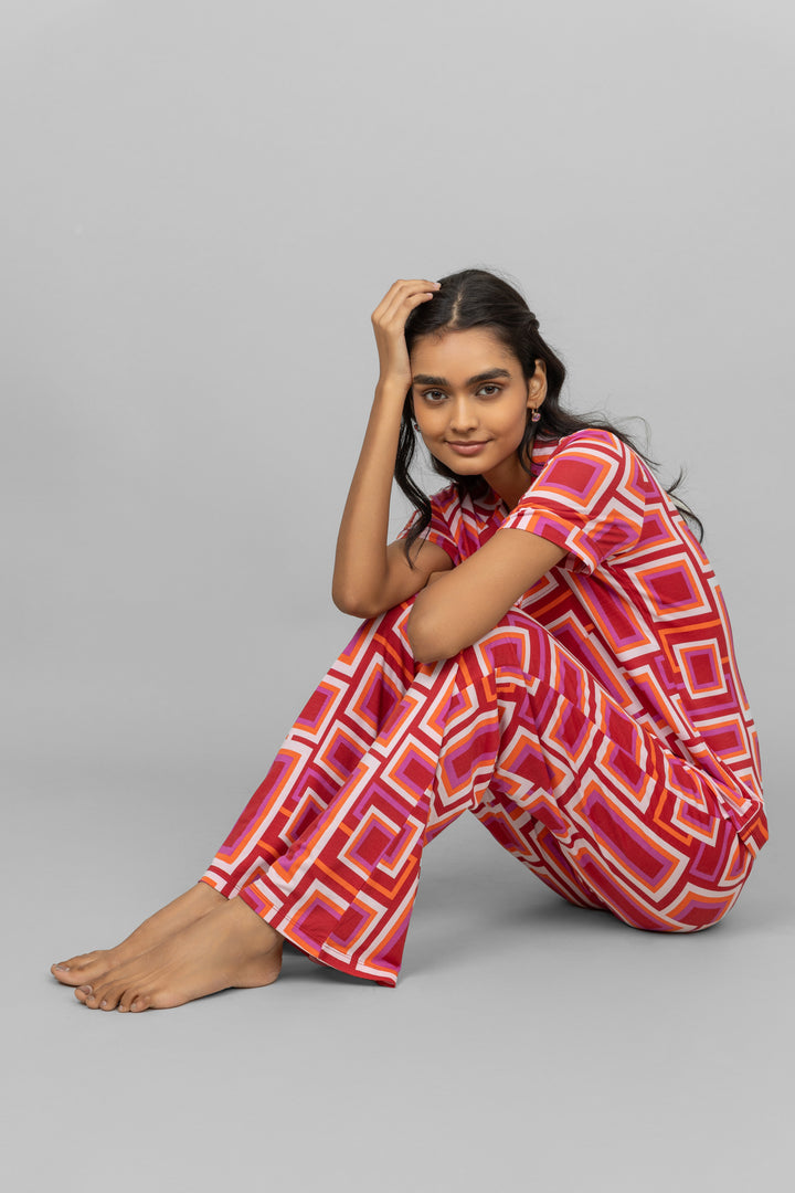 Stylish woman in red geometric pajama set sitting comfortably.