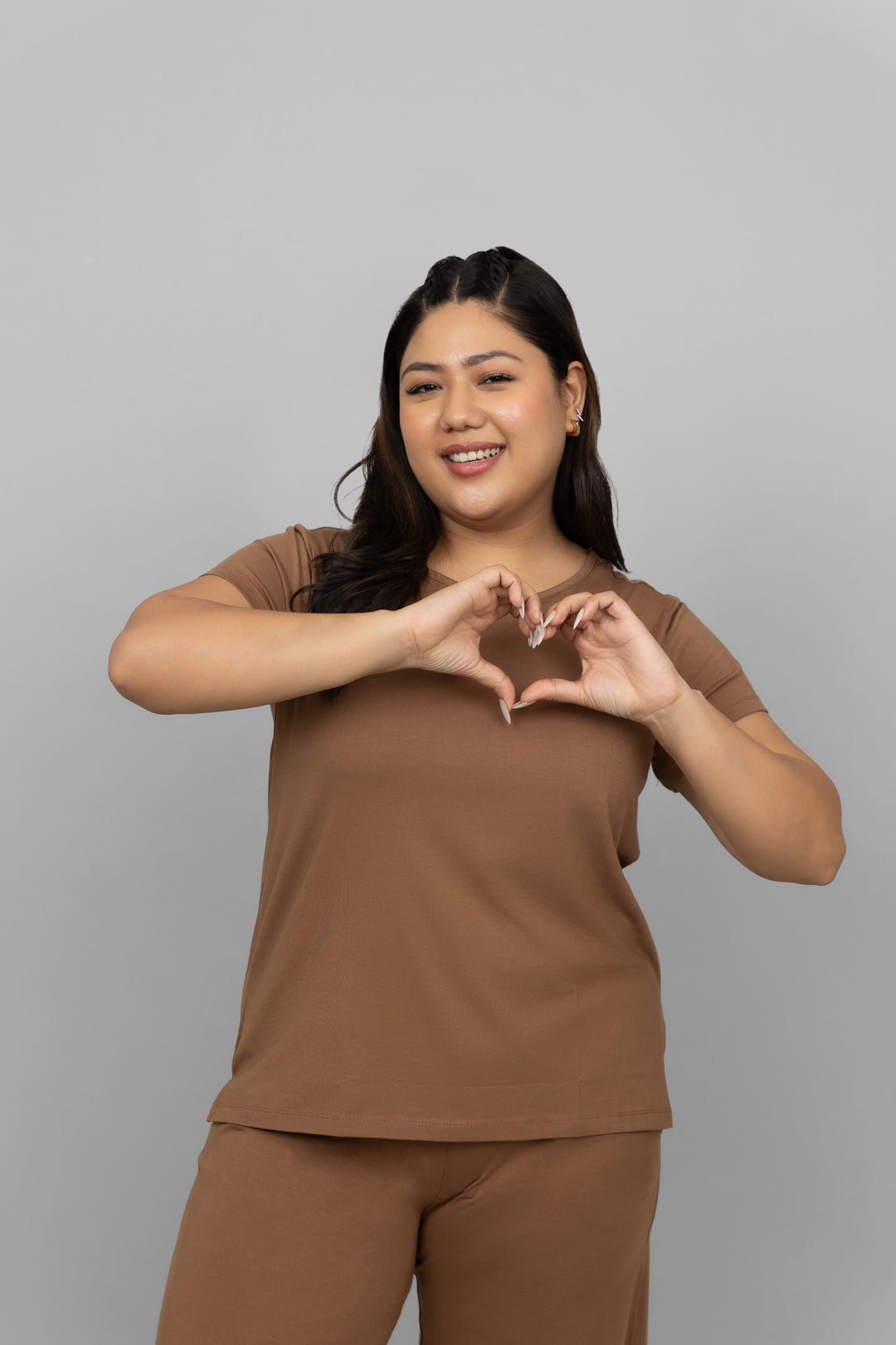 Smiling woman in brown round neck top making heart gesture.