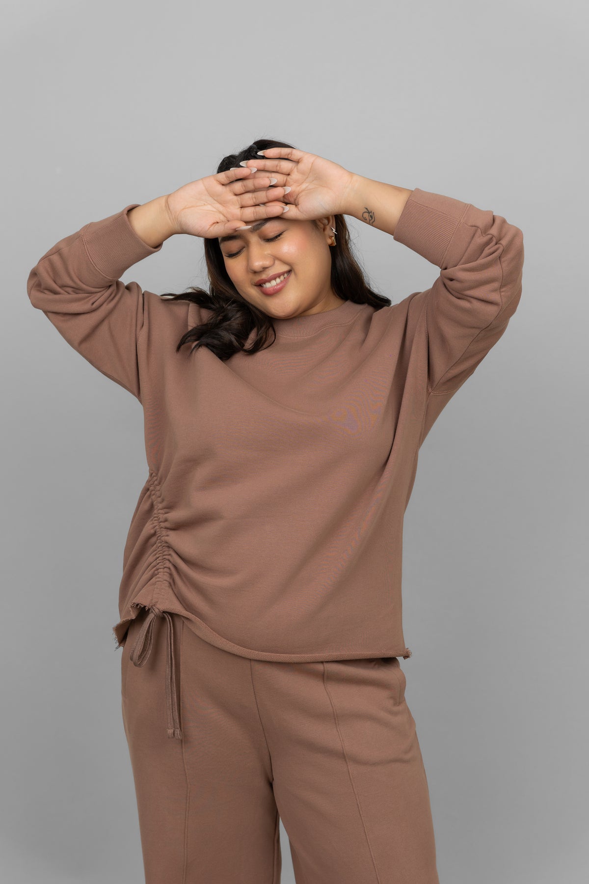 Woman smiling in a brown cotton terry sweatshirt, styled casually.