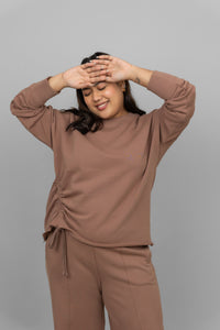 Woman smiling in a brown cotton terry sweatshirt, styled casually.