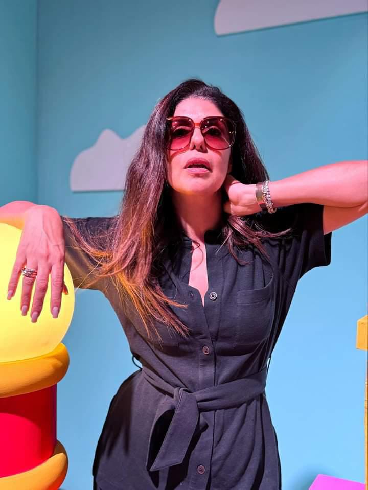 Stylish woman in black dress with sunglasses against vibrant backdrop.