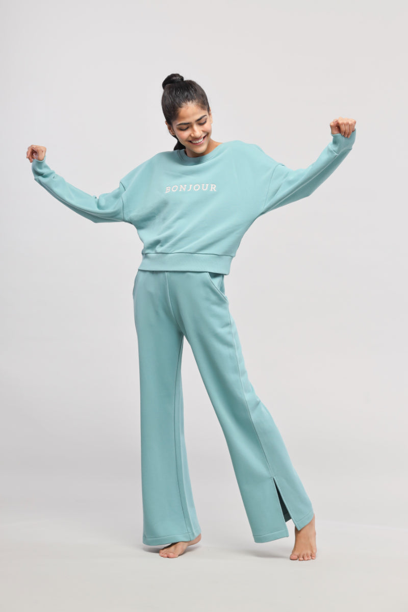 Woman wearing light blue Bonjour Terry Sweatshirt and pants, cheerful pose.