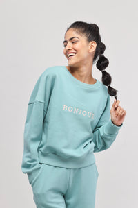 Woman wearing mint green Bonjour Terry Sweatshirt, smiling joyfully.