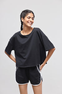 Boxy black cotton top worn with casual shorts, smiling model.