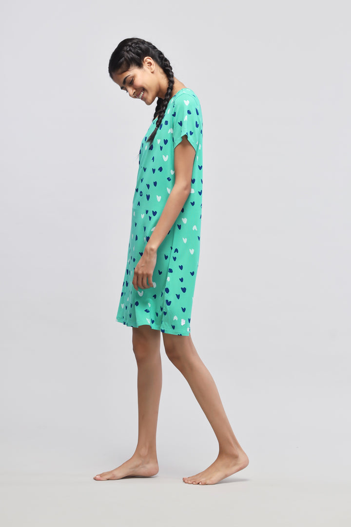 Model wearing Heartsy short dress with heart patterns, green background.