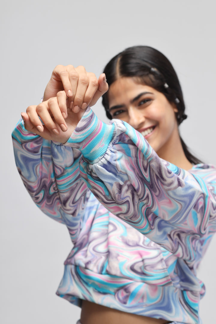 Fluid Terry Hoodie model showcasing colorful, marbled design with playful pose.