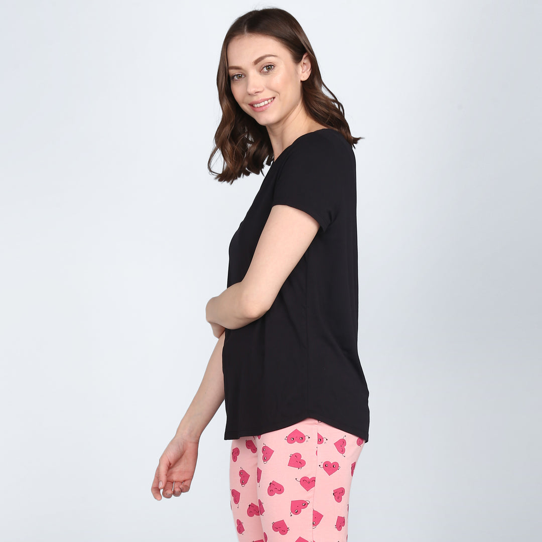 Model in black pajama set with playful pink heart-patterned pants.