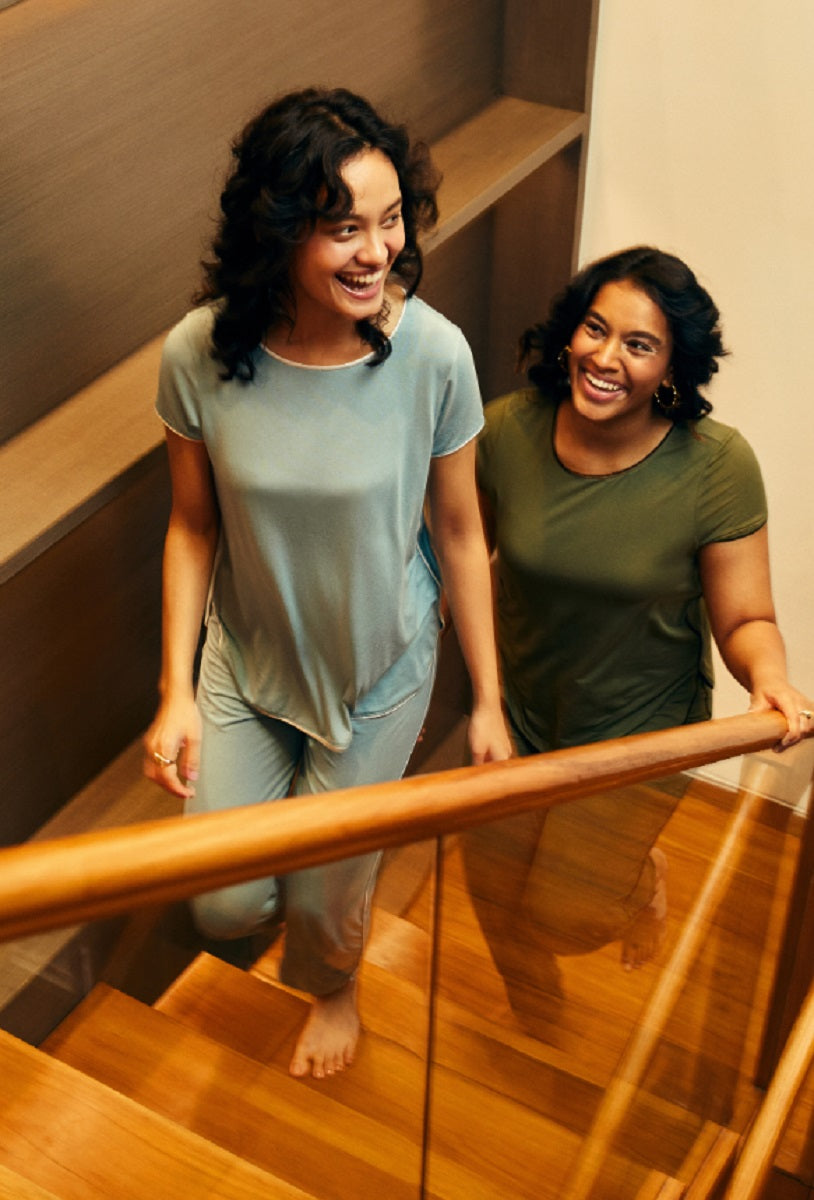 Two women smiling while wearing a delicate teal piping top.