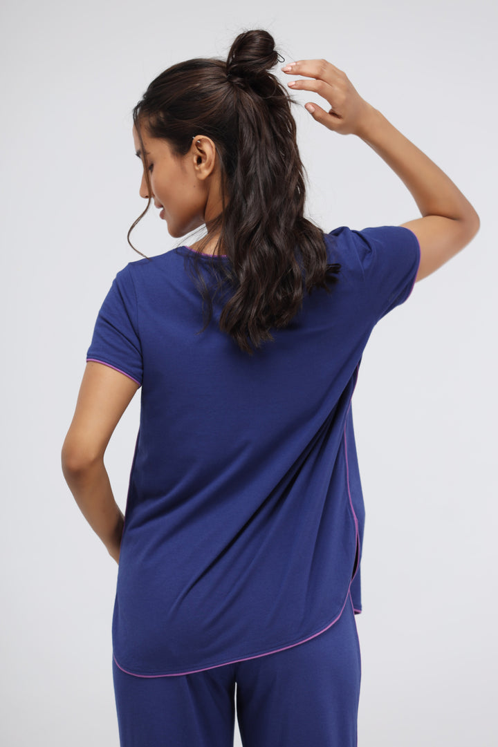 Woman in blue Supima® pajama set with pink piping, back view.
