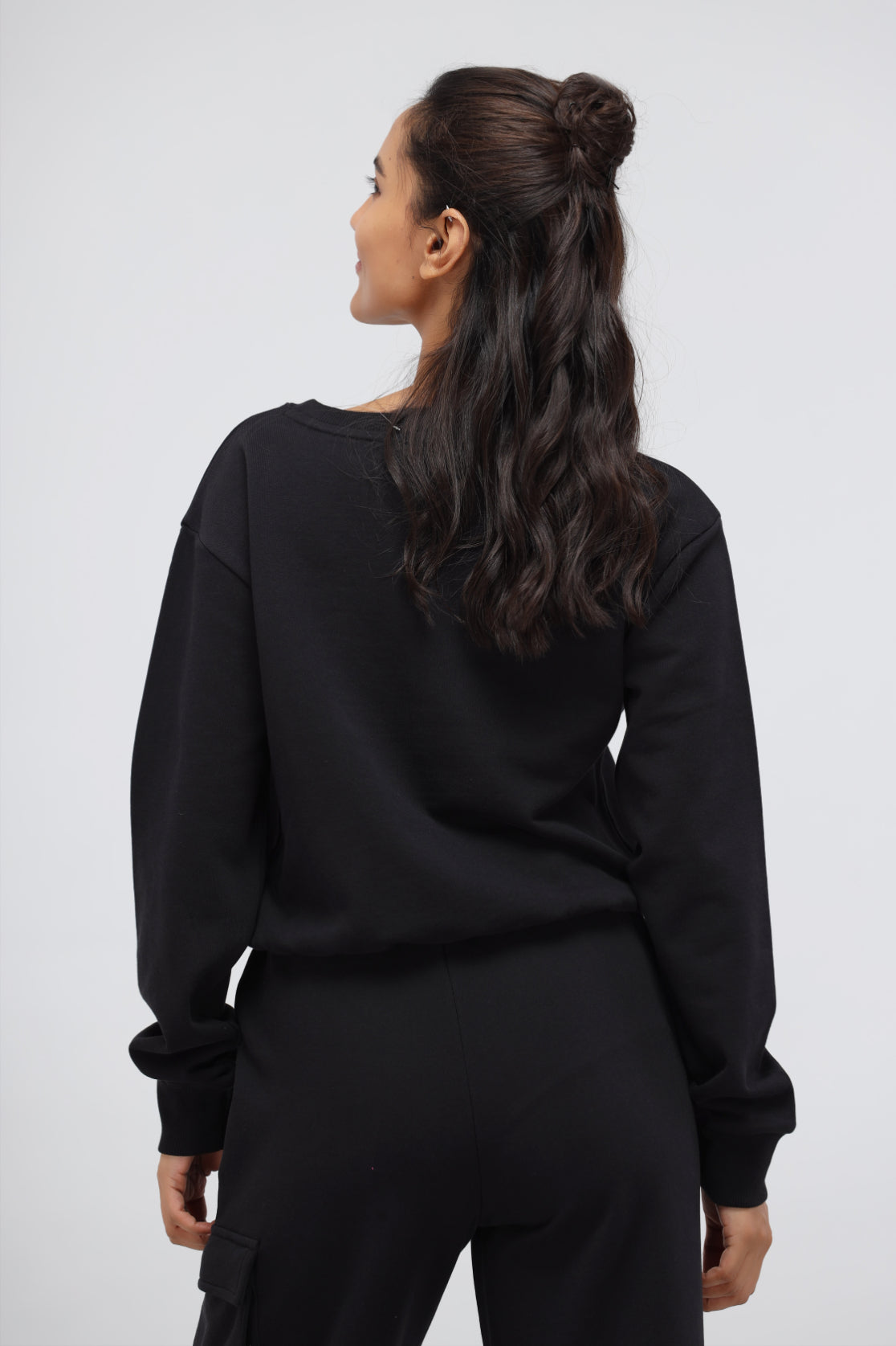 Woman wearing a jet black terry relaxed sweatshirt from the back.