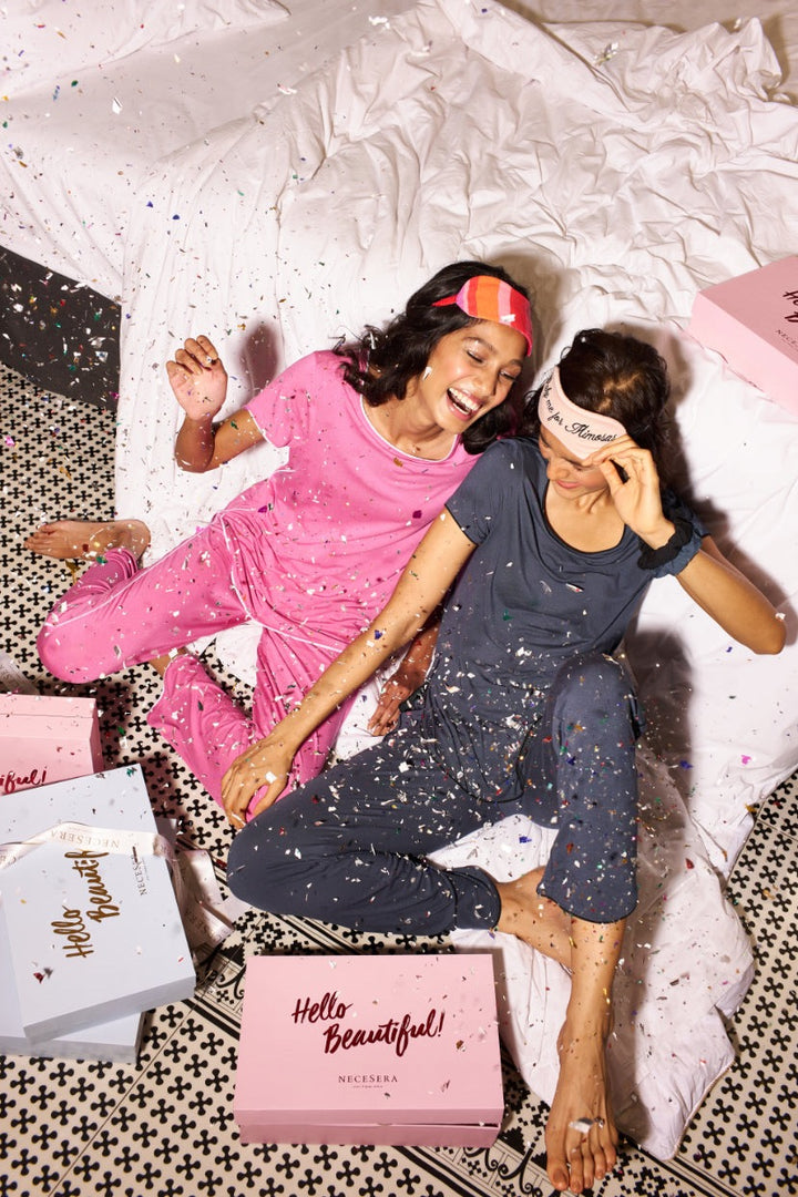 Women celebrating in rose pink and deep blue pajamas, festive atmosphere.